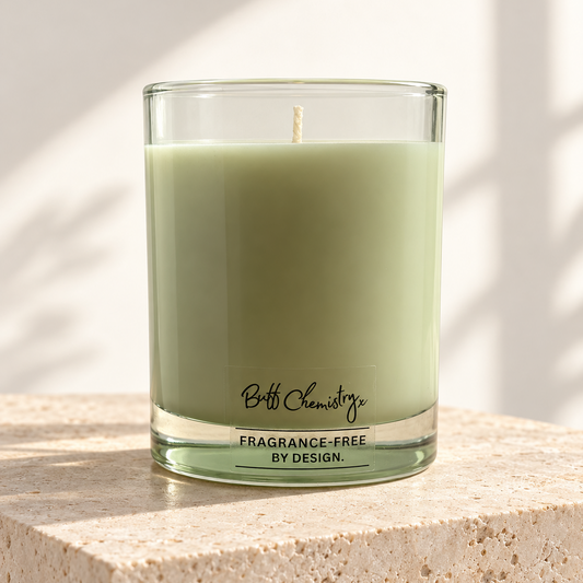 A green glass jar candle sits on a textured beige stone pedestal. The brand name 'Buff Chemistry' and 'Fragrance-Free by design' is printed in black script on the lower front of the glass.
