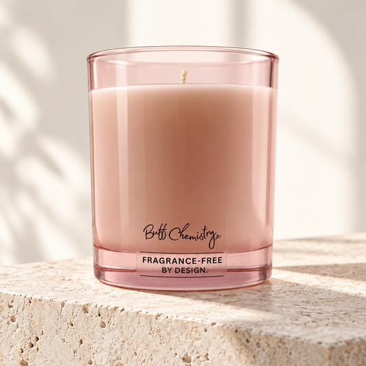 A pink glass candle from Buff Chemistry sits on a textured stone surface, with soft shadow patterns cast across the background.