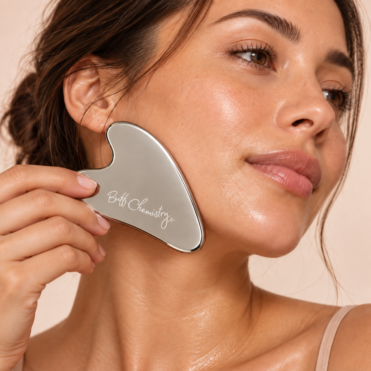 Woman using a Buff Chemistry stainless-steel Gua Sha tool along her jawline.